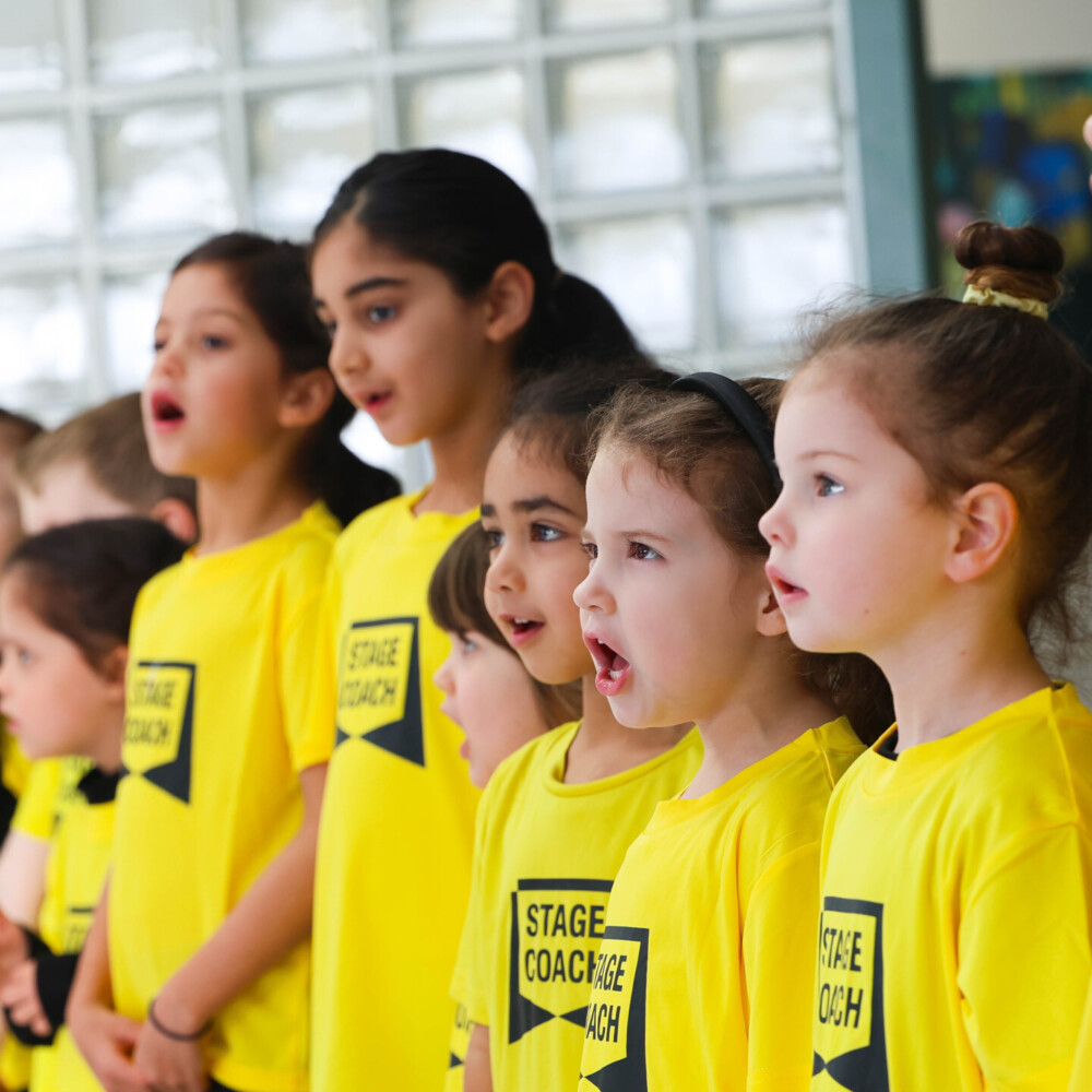 Row of Early Stages children in yellow Stagecoach T-shirts singing together