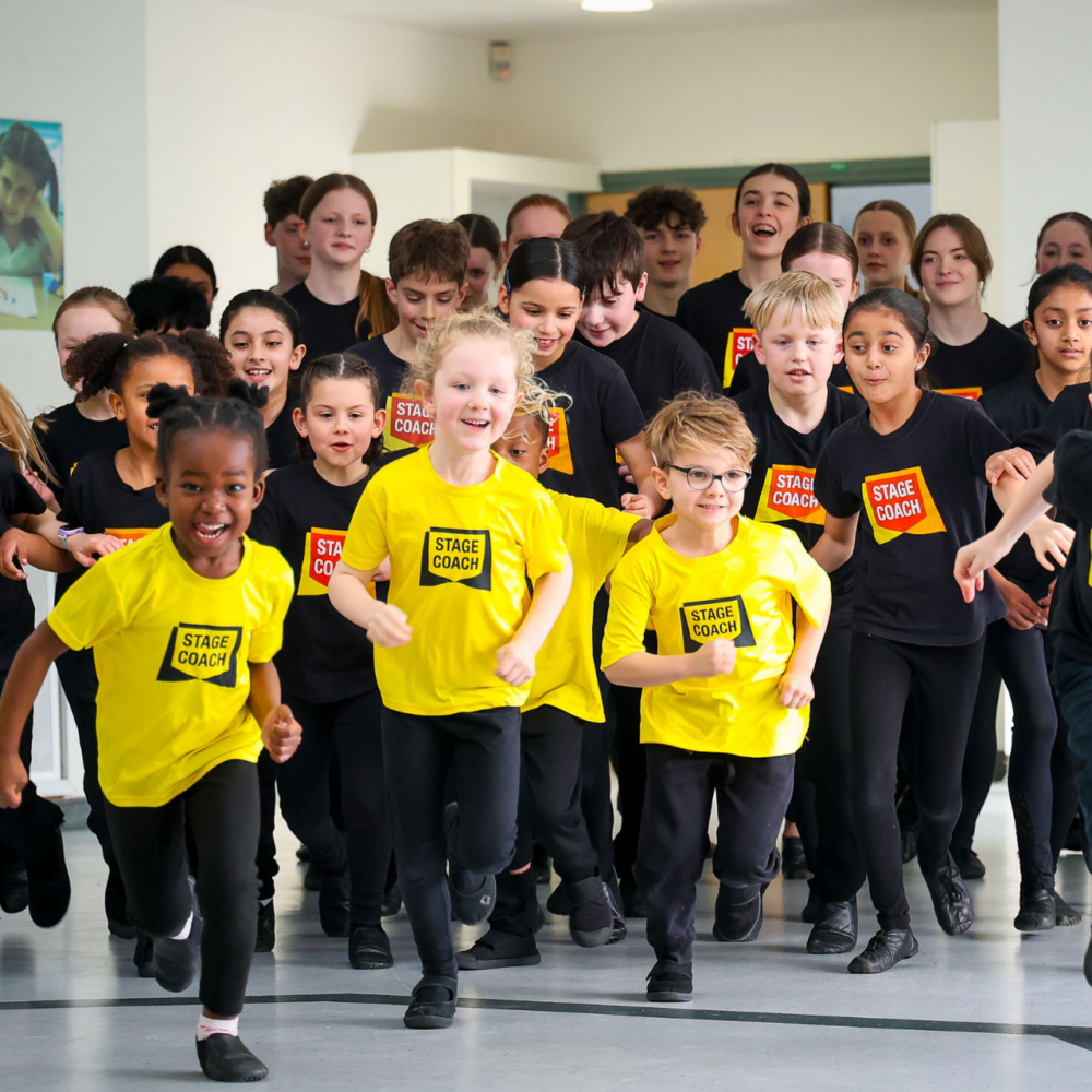 A joyful group of Stagecoach students in black and yellow uniforms running toward the camera during a performing arts activity.