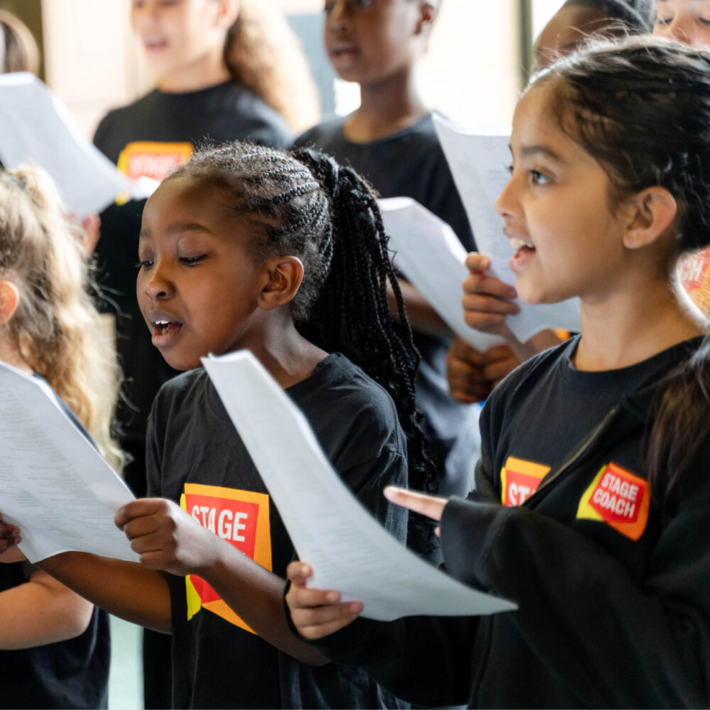 Young Stagecoach students singing from song sheets in class